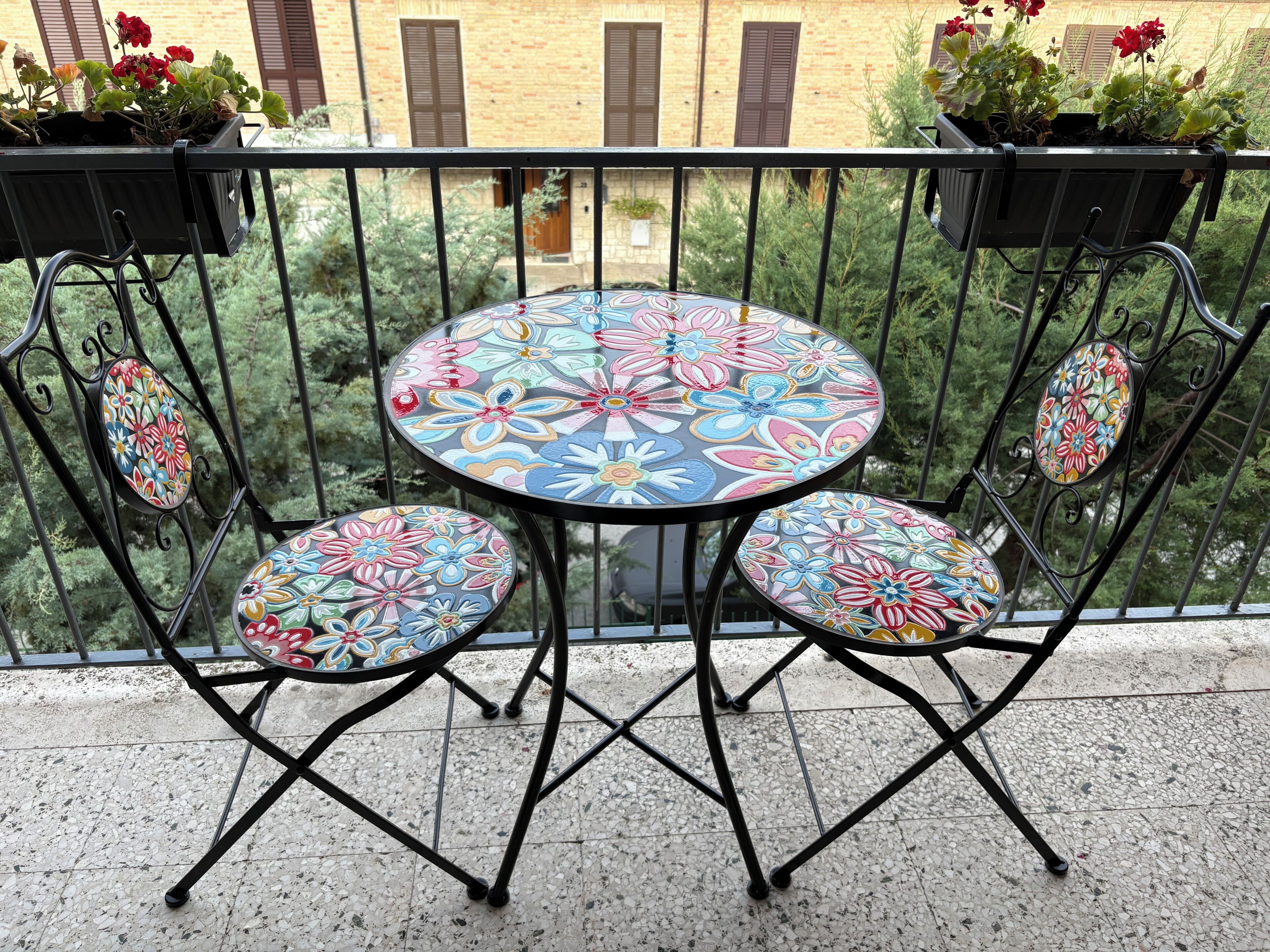 Un balcon avec une table ronde et des chaises, entouré d’une rambarde en métal.