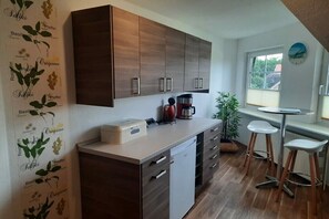 A compact kitchen with wooden cabinets, a countertop with a coffee maker, and a small dining area with stools. - Holiday apartment in Büsum with swimming pool (Büsum)