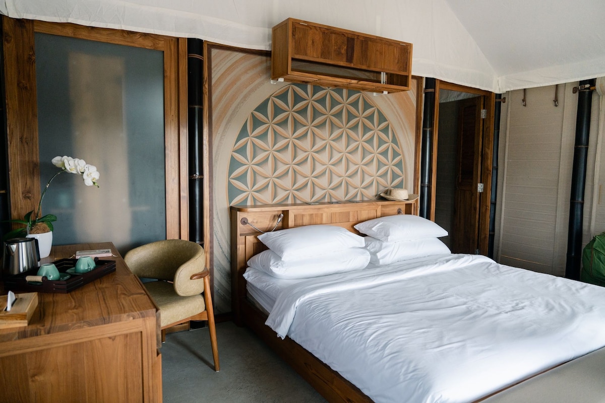 Une chambre à coucher avec une tête de lit en bois, un lit recouvert de linge de lit blanc, un bureau en bois, une chaise et un pot d’orchidée.