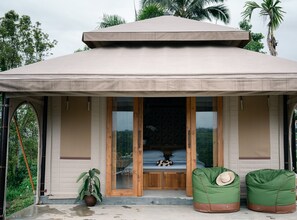Un espace extérieur abrité, doté d’une porte en bois, d’un petit coin salon avec un chapeau et d’une plante en pot.
