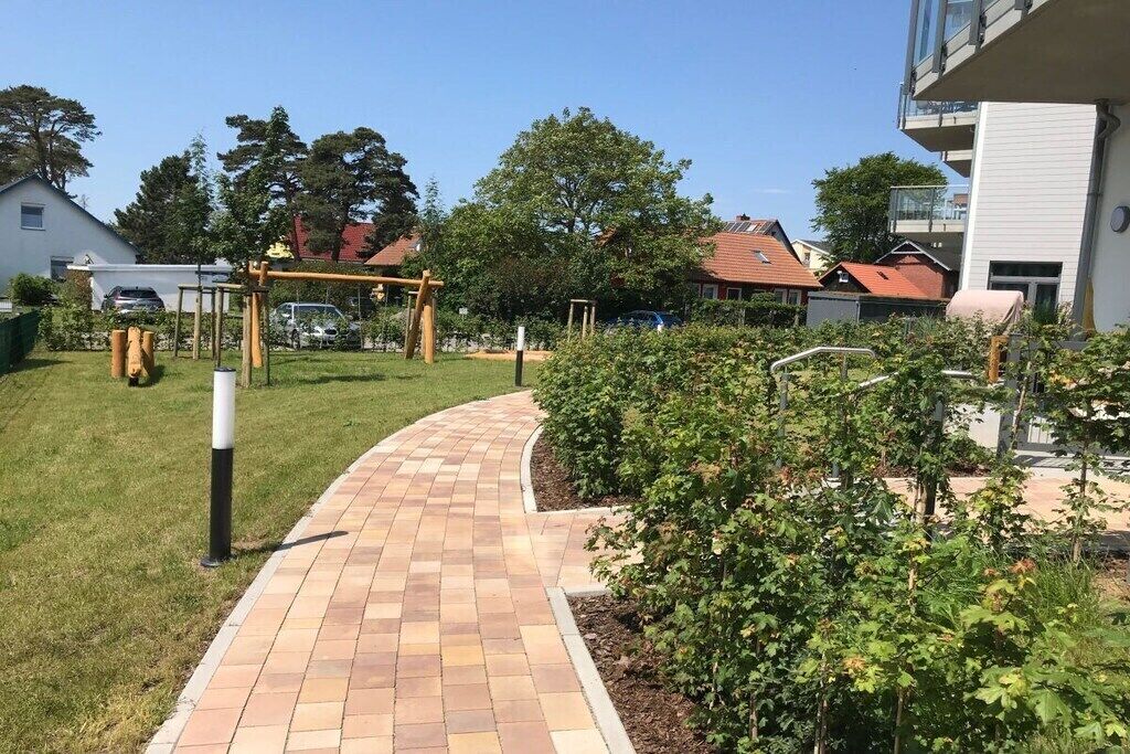 A paved pathway leading through a garden area with a wooden swing set and a small fence.