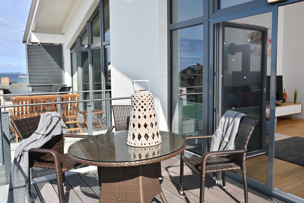 A balcony with wicker furniture, a glass table, and a decorative vase.