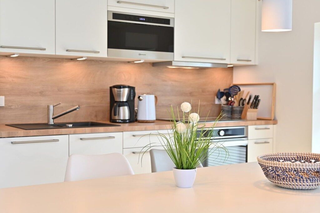 A modern kitchen with white cabinets, stainless steel appliances, and a wooden backsplash.