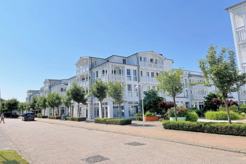 A multi-story residential building with balconies, a paved driveway, and landscaped areas with trees and shrubs.