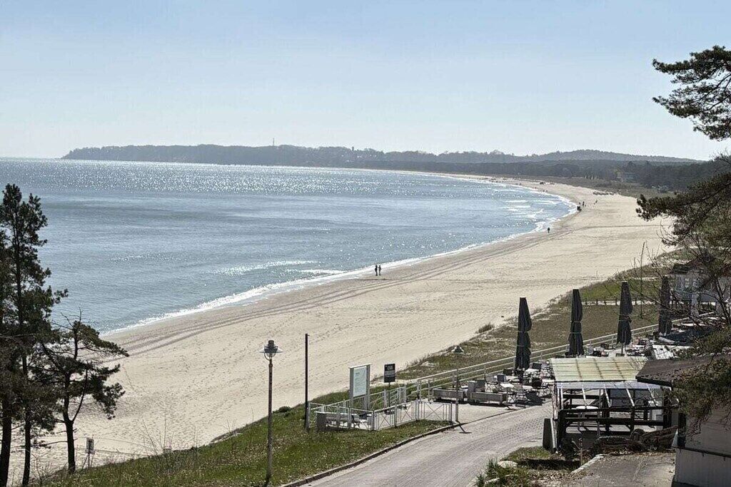 Une plage offrant une vue dégagée sur l’océan, une rive sablonneuse et une route menant à un bâtiment doté d’une terrasse.