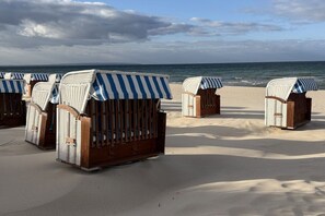 Strandliegen mit gestreiften Sonnenschirmen, auf einem Sandstrand mit dem Meer im Hintergrund.