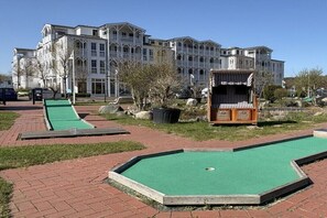 A courtyard with a green croquet field, a wooden gazebo, and a large building with multiple balconies in the background. - Holiday apartment "Little Seagull" (Ostseebad Sellin)
