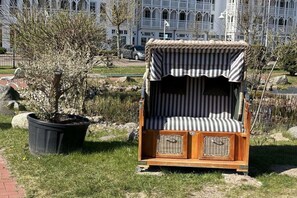 Un espace extérieur aménagé avec des sièges en bois, surmonté d’un auvent à rayures, agrémenté d’un panier en osier et d’une plante en pot.