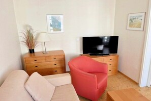 A living room with a sofa, a red chair, a TV on a wooden stand, a lamp, and two framed pictures on the wall. - Holiday apartment "Little Seagull" (Ostseebad Sellin)