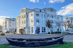 Un bâtiment blanc à la façade symétrique, doté de grandes fenêtres et d’une entrée centrale.