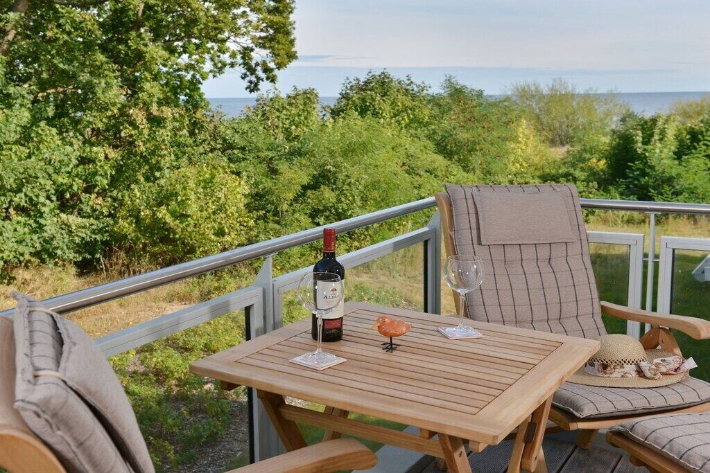 Een houten terras met een tafel, stoelen, een fles wijn en een glas.