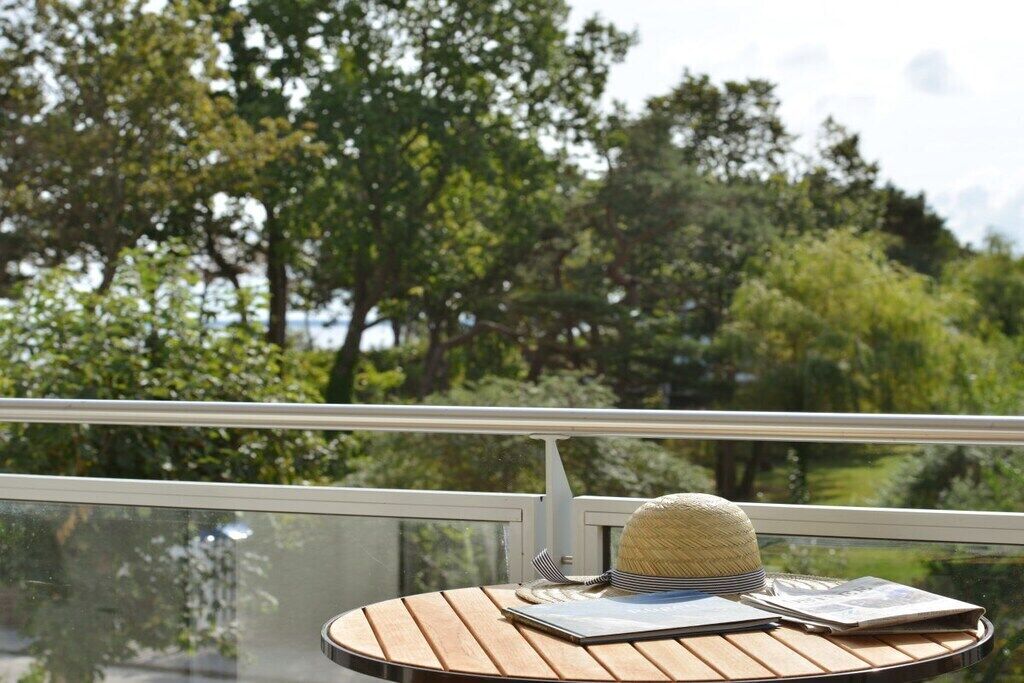Ein runder Holztisch mit einem Strohhut und einem Notizbuch, vor einer Glasbrüstung mit Blick auf eine üppige grüne Landschaft.