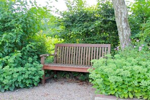 Eine hölzerne Bank in einem Garten mit üppiger Vegetation und einem Baumstamm.