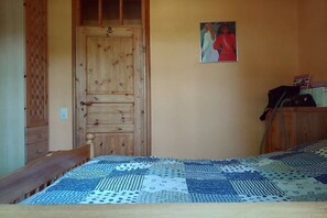 Ein Zimmer mit Holztür, einem Bett mit gemustertem Überwurf und einem an der Wand hängenden Bild.