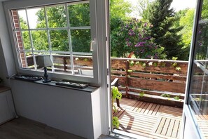 A room with a large window, a small table, and a view of a wooden deck with plants. - Wattenhuus Förrien 2a (Minsen - Förrien)