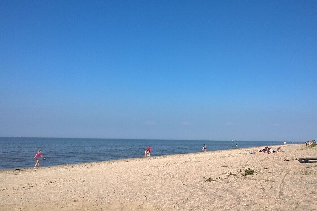 A beach with people walking and sitting on the sand, a clear sky, and the ocean in the background.