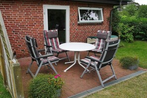 Eine Terrasse mit einer Ziegelmauer, einem weißen Tisch und vier Stühlen mit gestreiften Kissen.