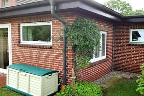 Een bakstenen huis met twee ramen, een groene schuur en een kleine tuin.