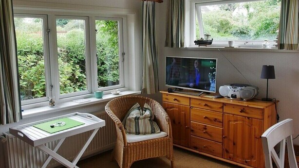 Ein Zimmer mit Fernseher, einem Korbstuhl, einem Holzschrank und einem fenster mit Vorhängen.