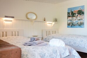 A hotel room with two beds, a painting of a harbor, a round mirror, and a small clock on the wall. - Terrace house by the sea (Langballig)