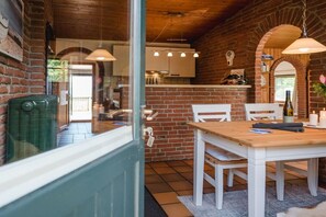 A rustic interior with a brick wall, wooden ceiling, and a dining area with white furniture. - Terrace house by the sea (Langballig)