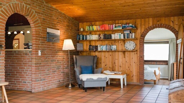 Ein gemütliches Zimmer mit Backsteinwand, Holzbalkendecke und einer Bücherwand voller Bücher.