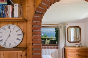A room with a wooden bookshelf, a large wall clock, a wooden dresser, and a view of a body of water through a window. - Terrace house by the sea (Langballig)