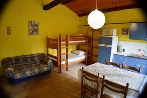 A compact room with bunk beds, a sofa, a dining table, and a kitchen area.