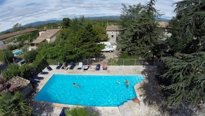 A rectangular swimming pool with a stone border, surrounded by lounge chairs and a fence. - Vrbo Property (Grospierres)