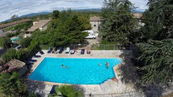 Piscina retangular com borda de pedra, rodeada por espreguiçadeiras e um cercado.