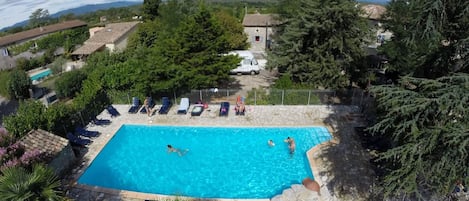 En rektangulär swimmingpool med en kant av sten, omgiven av solstolar och ett staket.