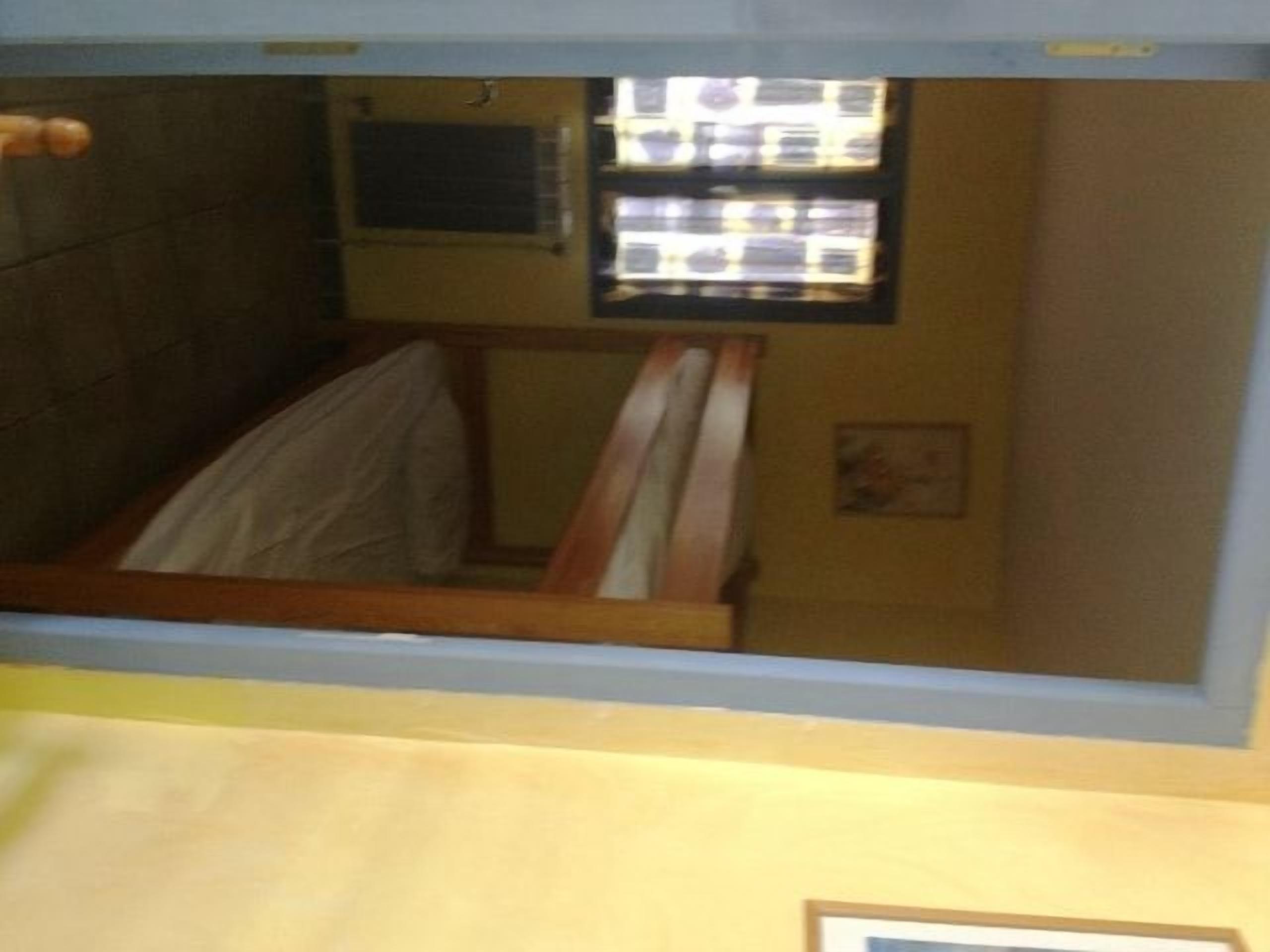 A room with a bed, a window with blinds, and a wall-mounted air conditioning unit.