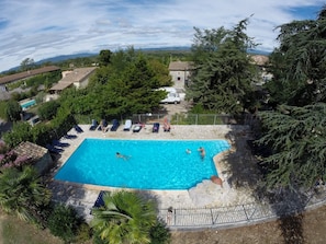 Piscina retangular com borda de pedra, rodeada por espreguiçadeiras e um cercado.