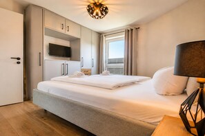 Une chambre d’hôtel avec un lit, une télévision, un bureau avec une lampe et une fenêtre avec des rideaux.