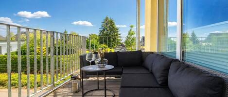 Un balcon avec un canapé noir, une table ronde et un verre de vin.