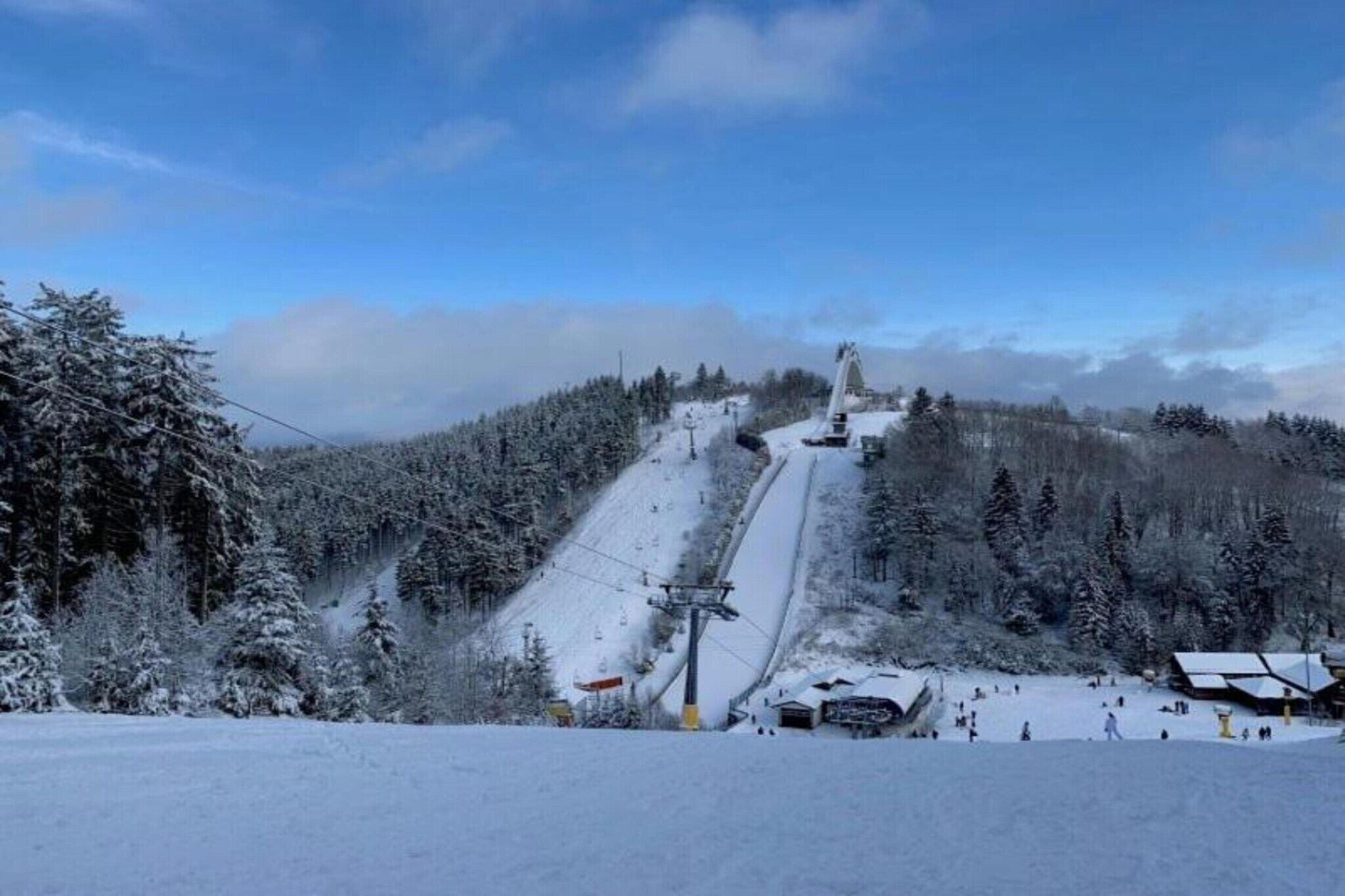 A snow-covered ski slope with a ski lift and a small building at the bottom.