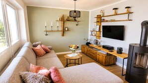 Ein Wohnzimmer mit einer Couch, einem Couchtisch, einem Fernseher, einem Kamin und Holzregalen mit Dekorationselementen.
