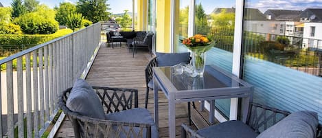 A balcony with a table and chairs, a vase with flowers, and a view of the neighborhood.