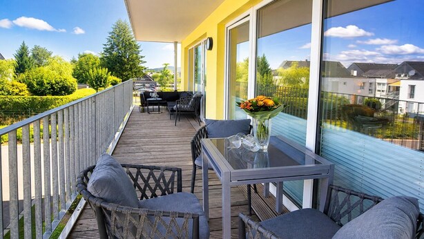 Ein Balkon mit Tisch und Stühlen, einer Blumenvase und Blick auf die Nachbarschaft.