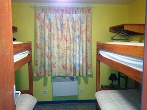 Ein Zimmer mit Etagenbetten, einem Vorhangfenster, einem Heizgerät und einem kleinen Tisch mit Lampe.