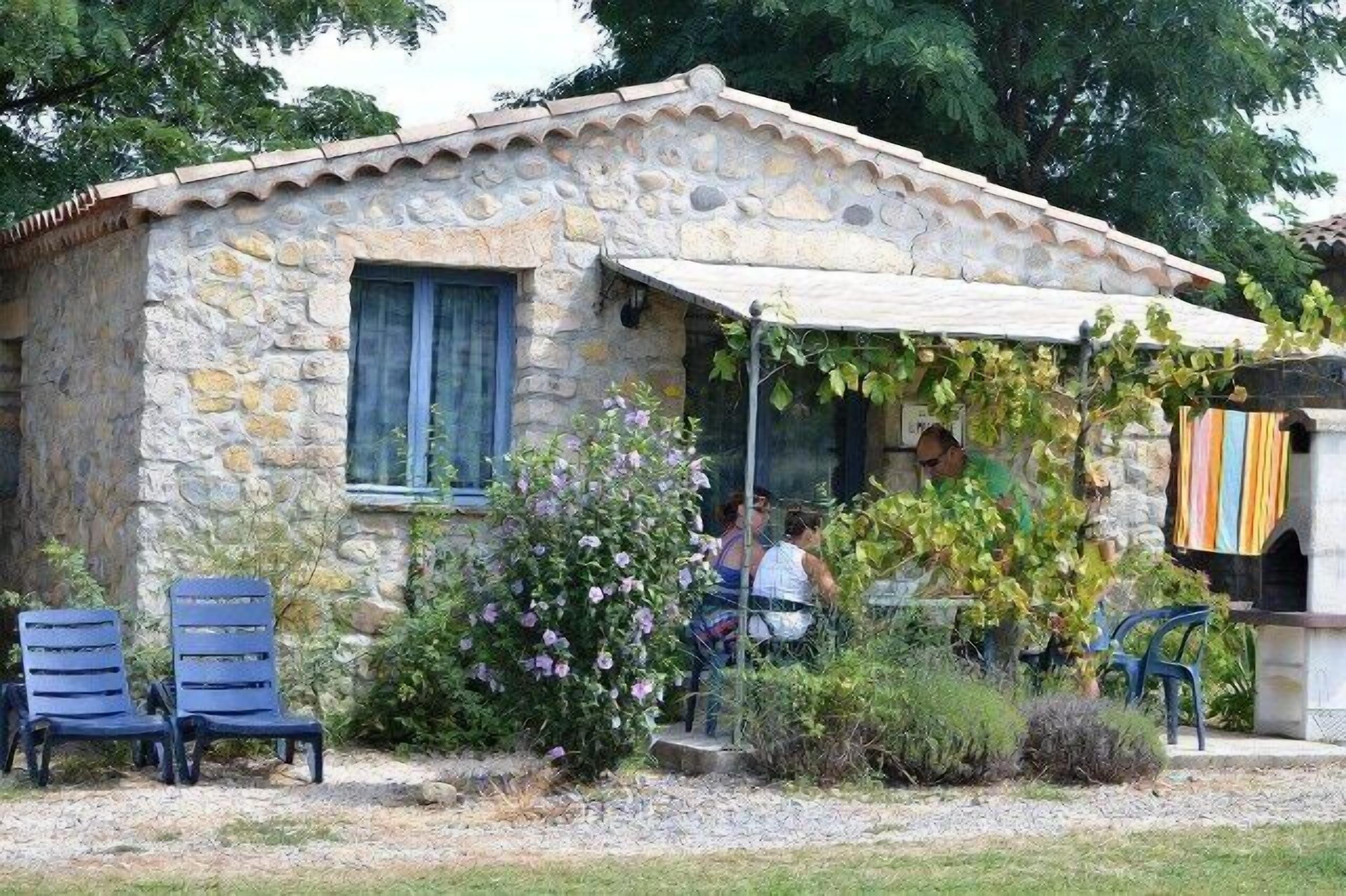 Ein Steingebäude mit einer Veranda, Sitzgelegenheiten im Freien und einem Garten.