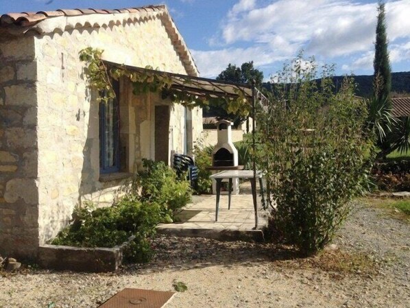 Un edificio de piedra con tejado de baldosas, un espacio cubierto para sentarse al aire libre y un pequeño jardín con un camino de grava.