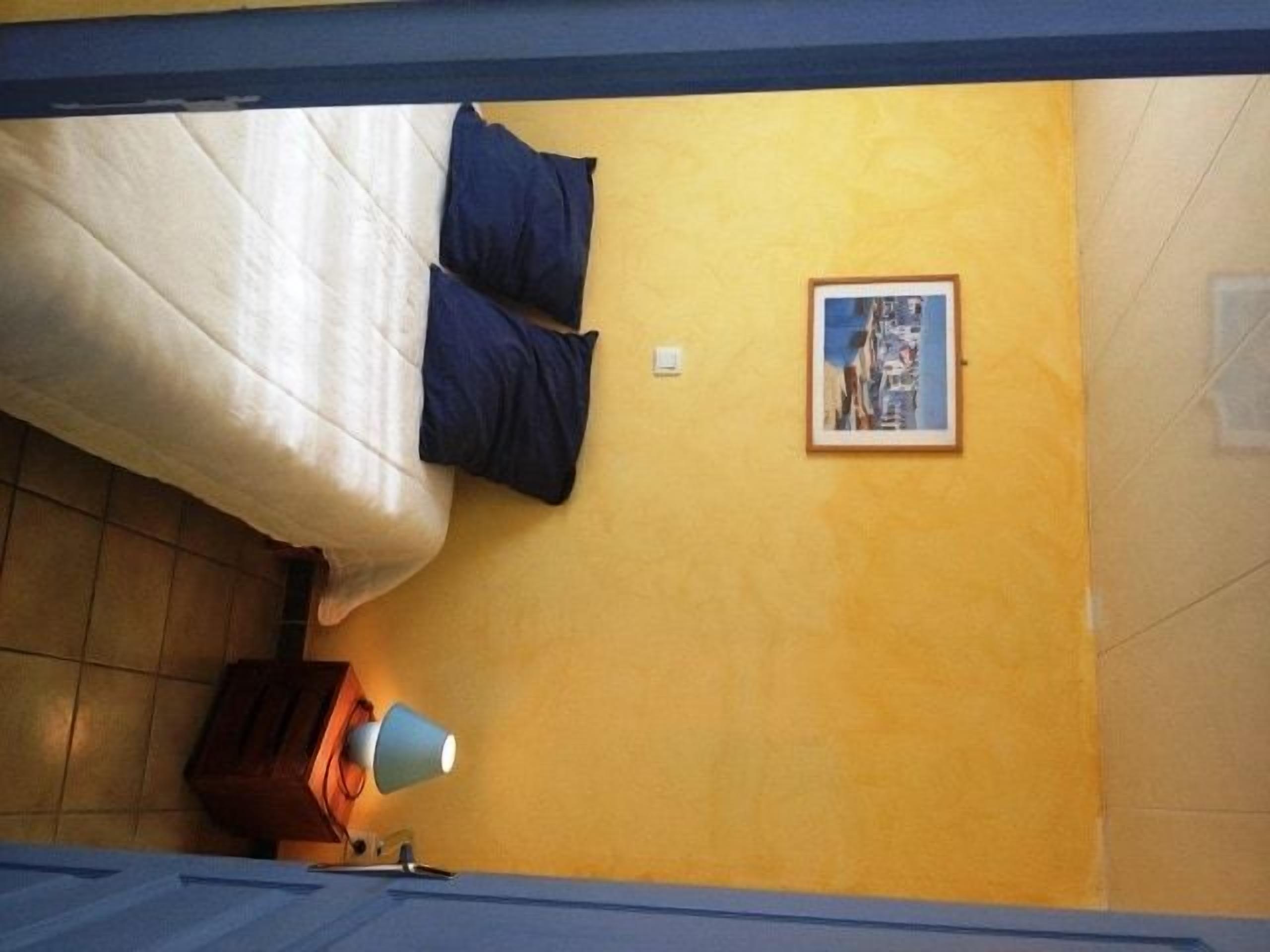 Ein Zimmer mit einem Bett, einer Lampe, einem gerahmten Bild an der Wand und einem Holzschrank.