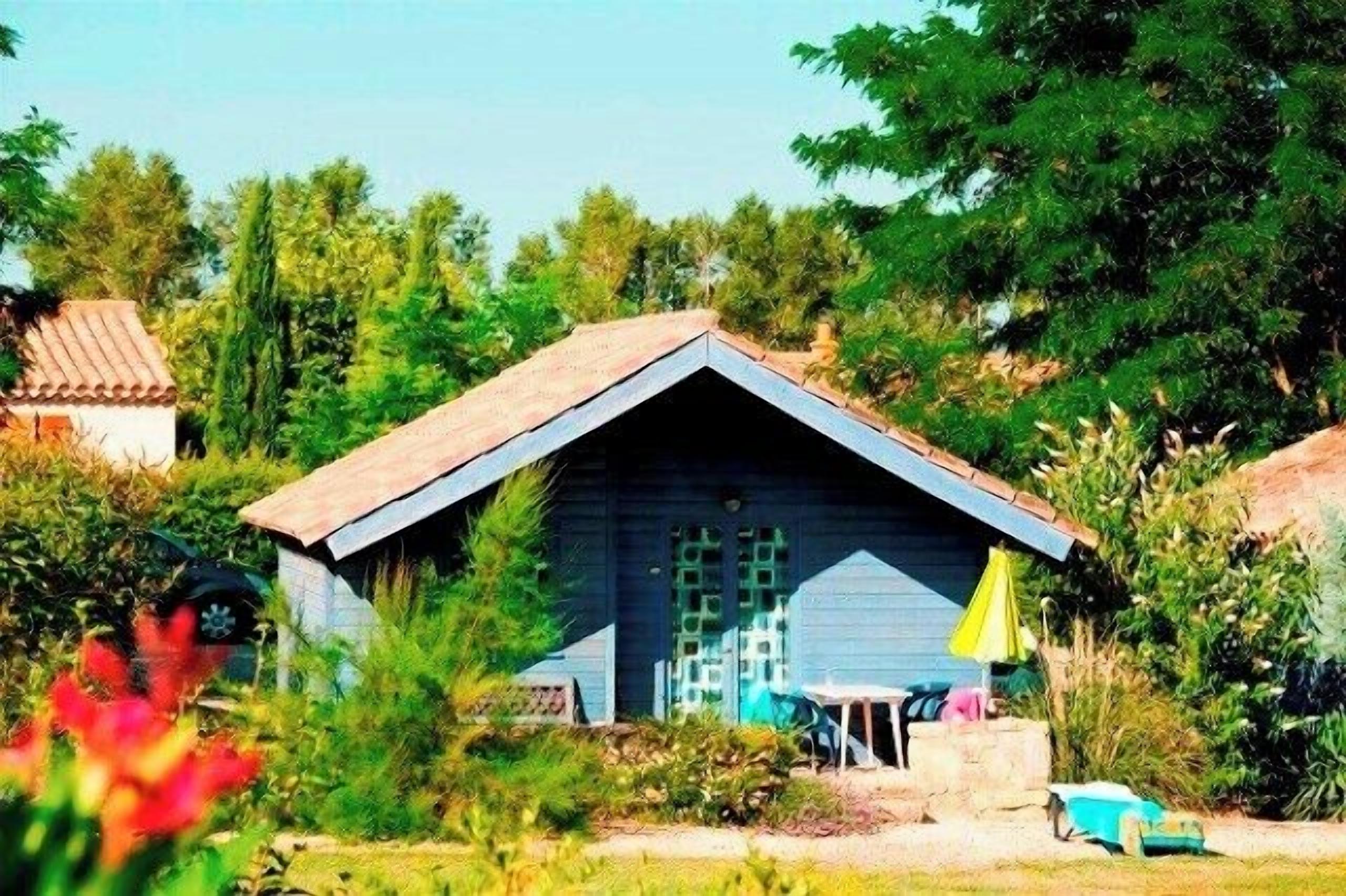 A rustic wooden cabin with a pitched roof, surrounded by lush greenery and a clear sky.
