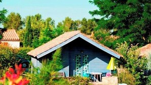A rustic wooden cabin with a pitched roof, surrounded by lush greenery and a clear sky. - Chalet #15, sleeps 4, Domaine de Ribière (Grospierres)