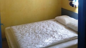 A single bed with a white mattress and pillows, a wooden ceiling, a yellow wall, and a colorful painting. - Chalet #15, sleeps 4, Domaine de Ribière (Grospierres)