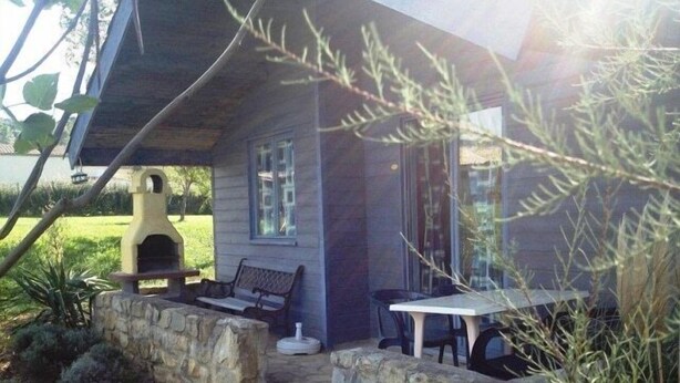 A stone-walled outdoor seating area with a bench and table, a barbecue grill, and a house with a window. - Chalet #15, sleeps 4, Domaine de Ribière (Grospierres)