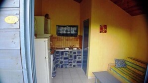 A compact kitchen with a sink, a small refrigerator, and a window above the counter. There is a bench with a cushion in the adjacent room. - Chalet #15, sleeps 4, Domaine de Ribière (Grospierres)