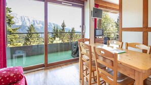A room with a dining table and chairs, a television, and a balcony with a mountain view. - Alpine Ski Apartment in Tignes for 4 (Chamrousse)