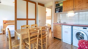 A compact kitchen with a washing machine, wooden cabinets, and a dining area with a table and chairs. - Alpine Ski Apartment in Tignes for 4 (Chamrousse)